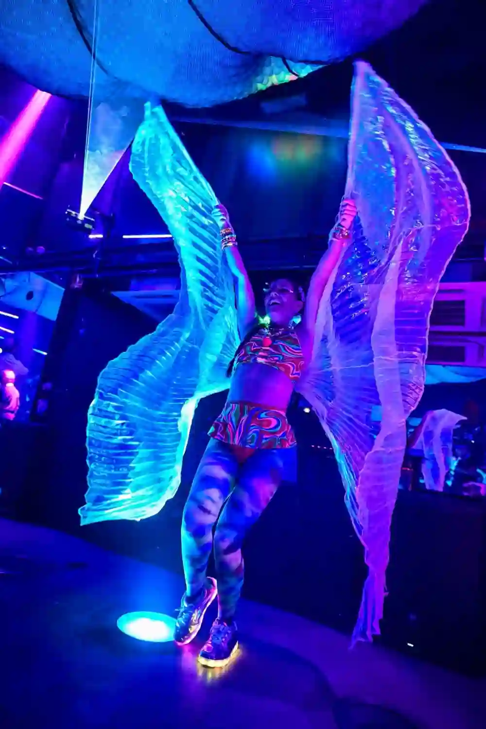 Performer in glowing wings under blue and violet light