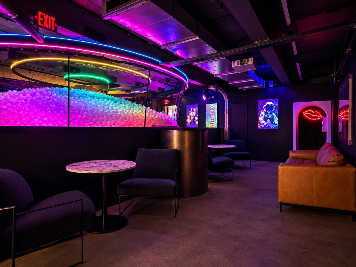 The lounge at The Drop PHX: a leather couch and neon wall art, looking down over the glowing ball pit