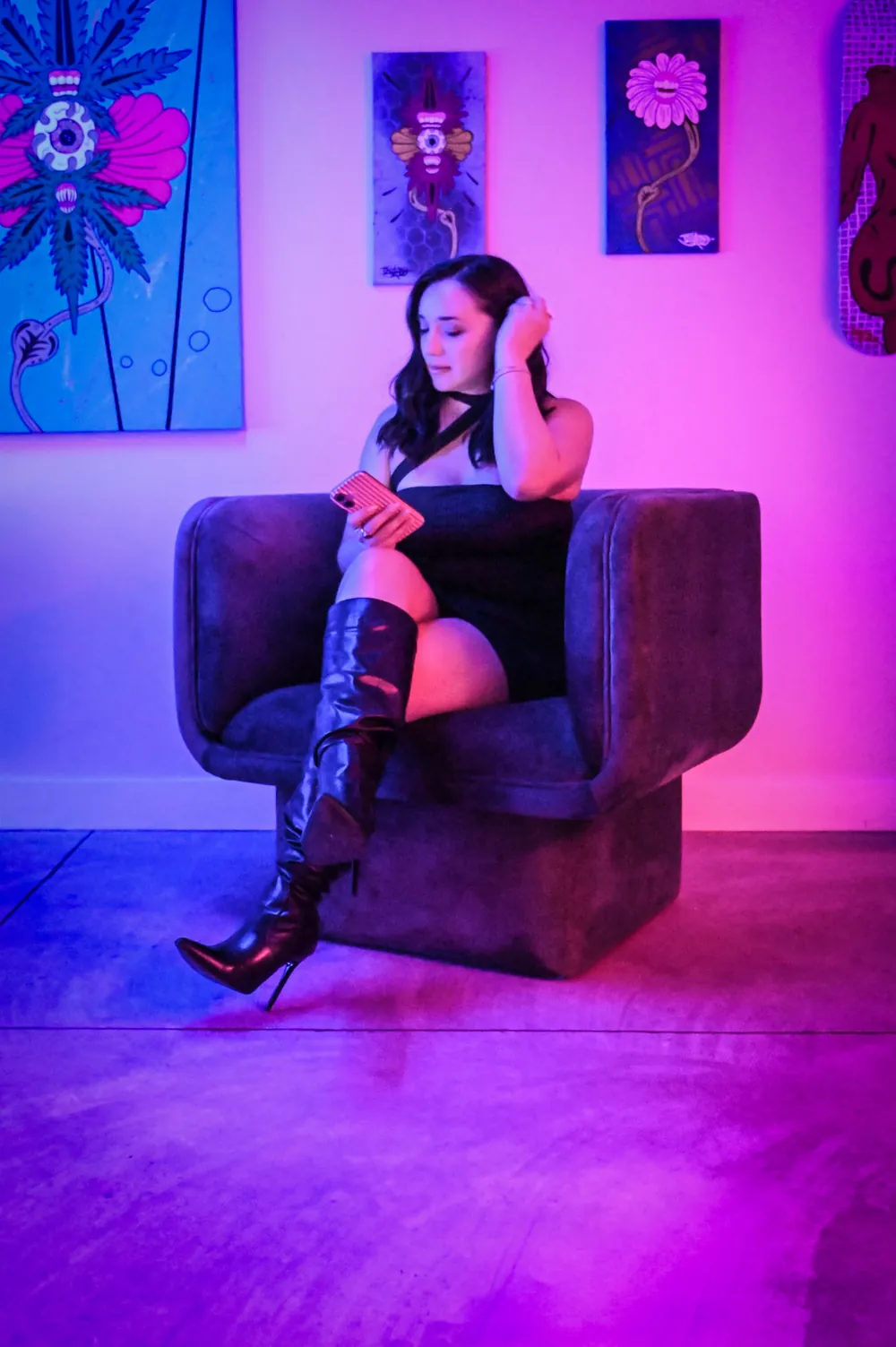 Model in a lounge chair under pink and blue RGB lighting in front of the art wall at The Drop PHX studio